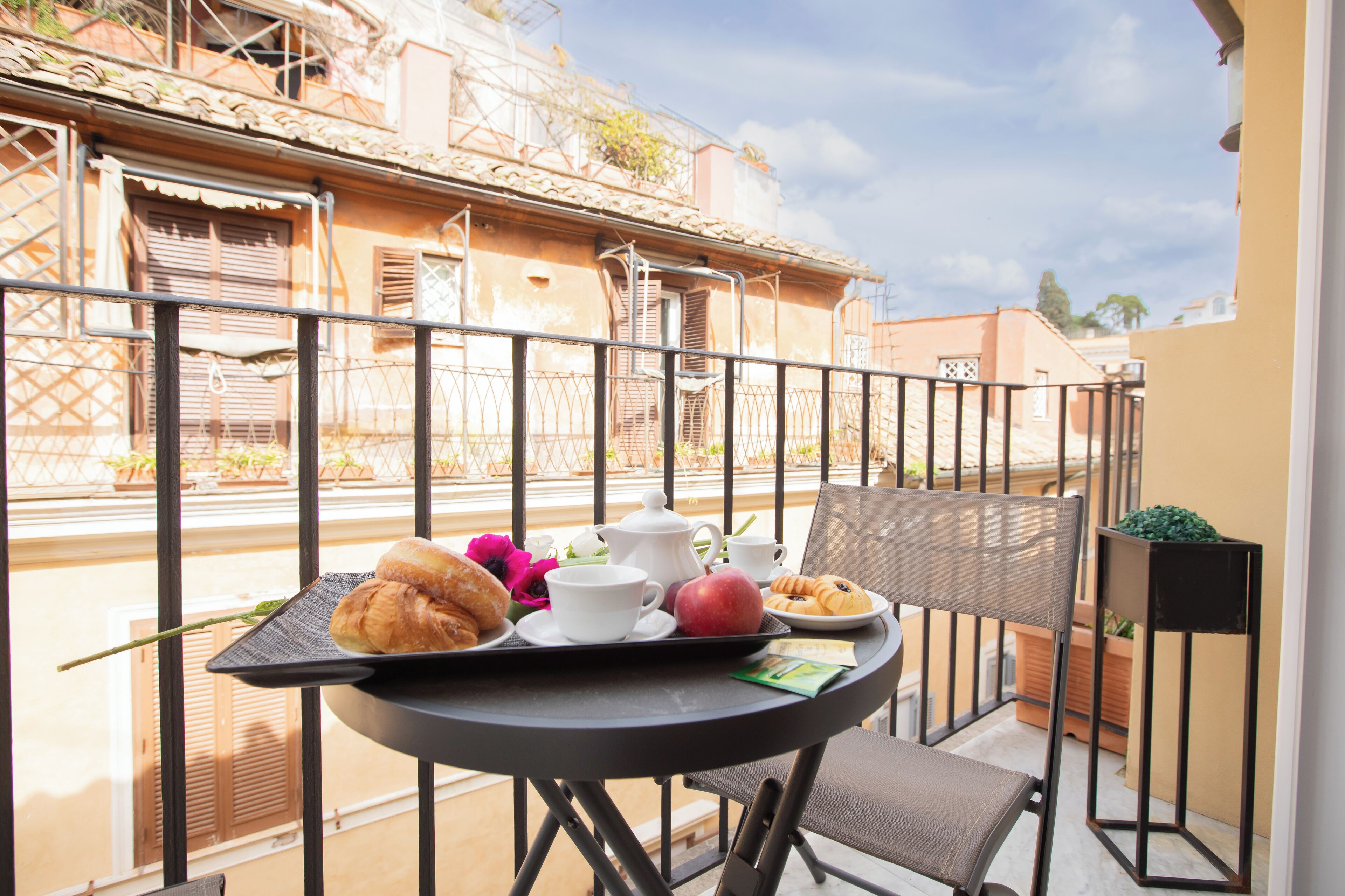 A balcony with a table set for breakfast, including croissants, a red apple, and a cup.