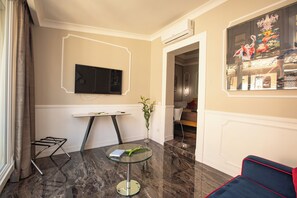 A modern hotel room with a marble floor, a glass table, a flat-screen TV mounted on the wall, and a view of a restaurant through a window. - Luxury Through the Ages   (Roma)