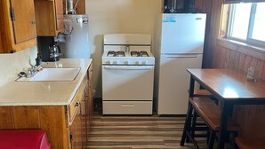 Une cuisine compacte avec des meubles de rangement en bois, une cuisinière à gaz, un réfrigérateur et une petite table à manger.