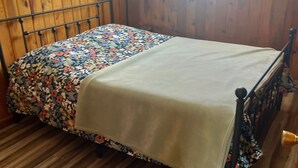 Une pièce aux murs lambrissés, avec un lit recouvert d’une courtepointe à motifs floraux et d’un drap blanc uni.