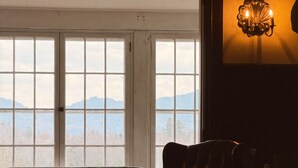 A room with a large window, a sofa, a chair, a lamp, and a small table. - Walk to Main Street & Mirror Lake (Lake Placid)