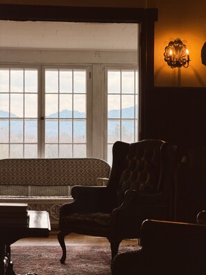 Ein Zimmer mit großem Fenster, einer Couch, einem Sessel, einer Lampe und einem kleinen Tisch.