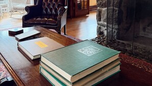 A cozy room with a stone fireplace, a leather armchair, and a table with books. - Walk to Main Street & Mirror Lake (Lake Placid)