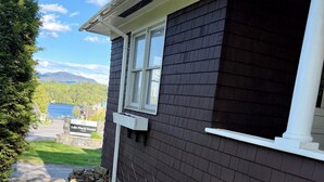 A dark-colored building with a white window, a driveway, and green plants along the side. - Walk to Main Street & Mirror Lake (Lake Placid)