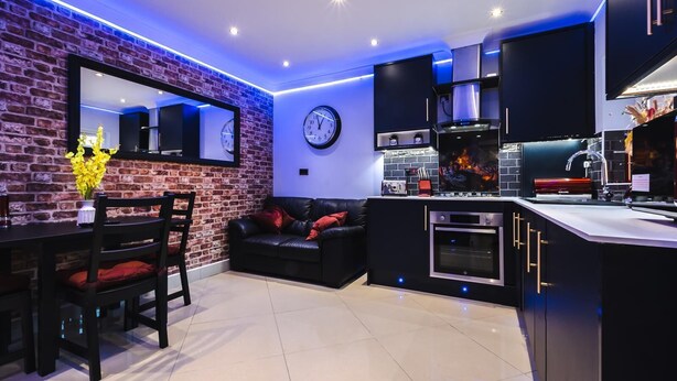 Een moderne keuken met een bakstenen muur, een zithoek met een zwarte leren bank en een inbouwoven.