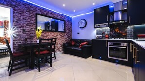 Een moderne keuken met een bakstenen muur, een zithoek met een tafel en stoelen, en een zwarte leren bank.