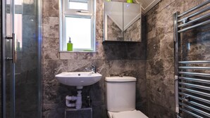 Een badkamer met een douchecabine van glas, een witte wastafel, een toilet en een handdoekrek.