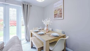 Een eetgedeelte met een houten tafel voor vier personen, een vaas met bloemen en een schilderij aan de muur.
