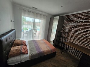 A bedroom with a bed, a brick wall, a sliding glass door, and a small table. - House 90 m2 with swimming pool and air conditioning - 3 bedrooms - near Montpellier (Grabels)