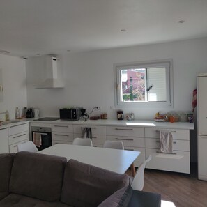 A modern kitchen with white cabinetry, a dining area with a brown sofa, and a window with a view of buildings outside. - House 90 m2 with swimming pool and air conditioning - 3 bedrooms - near Montpellier (Grabels)