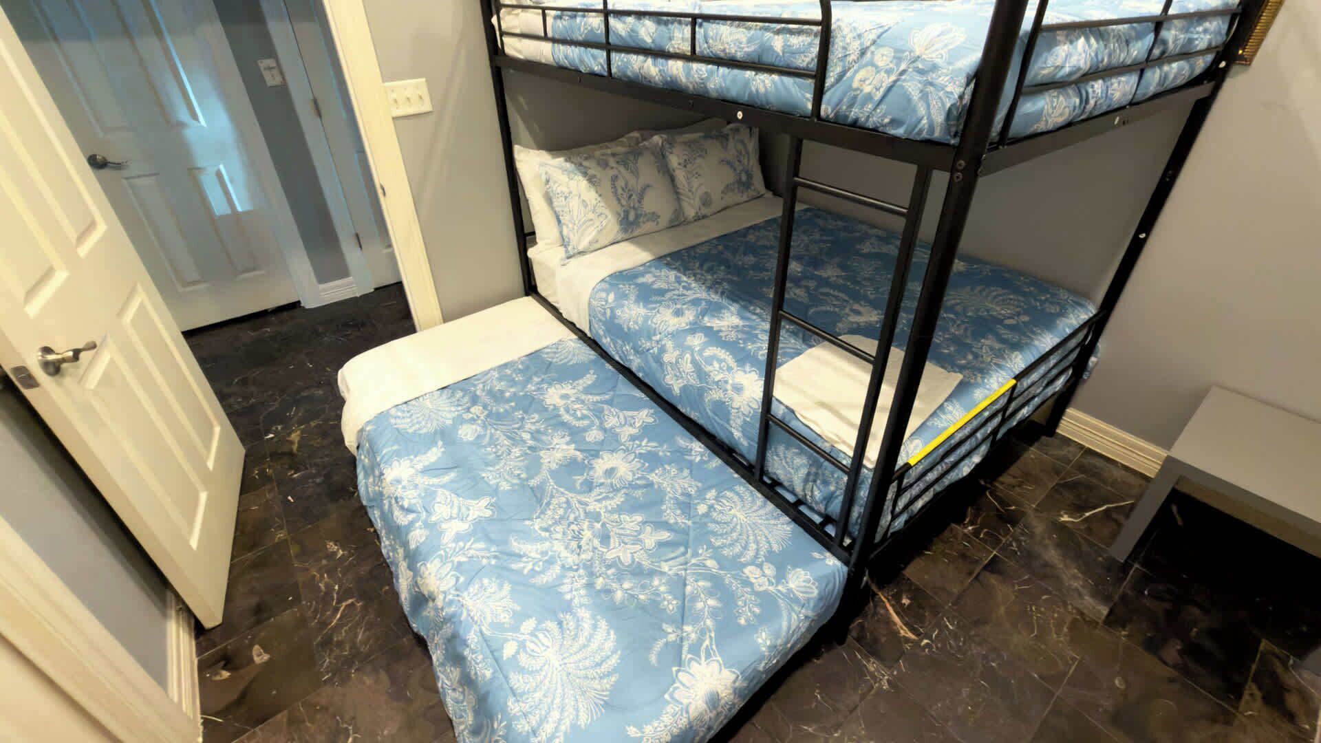 A bunk bed with floral bedding in a room with a tiled floor and a door in the background.