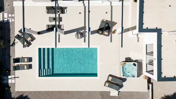 En vy från ovan av ett hotell med en stor pool, flera solstolar och en bubbelpool.