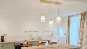 A kitchen with a central island, a stove, and a sink. There are hanging pendant lights above the island. - Bright English-style cottage apartment (Mazet-Saint-Voy)