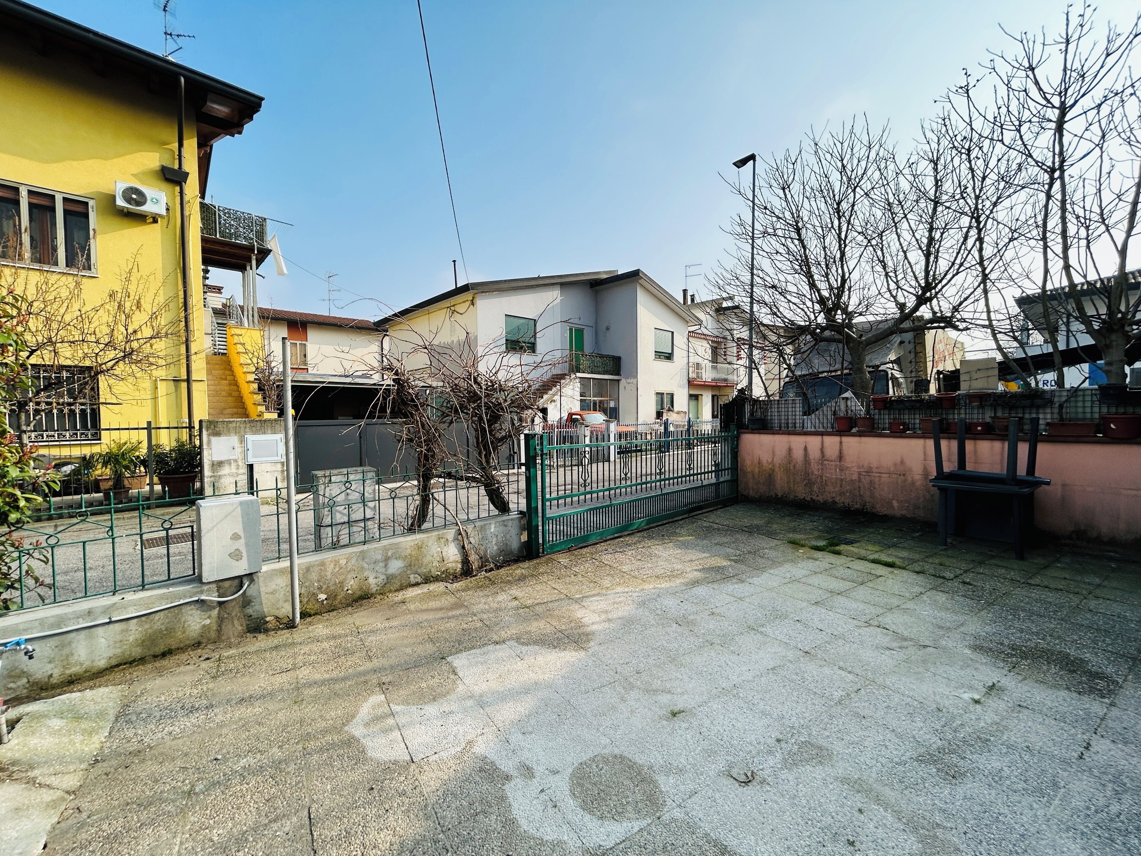 Zona residencial con entrada protegida por un portón, un edificio amarillo y otro blanco con balcón.