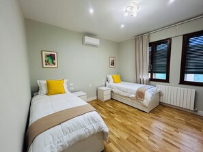 Een slaapkamer met twee bedden, een witte airconditioner, een radiator en een raam met jaloezieën.