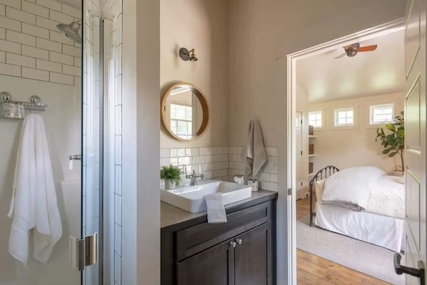 A bathroom with a glass shower, a sink with a mirror, and a towel hanging on the wall.