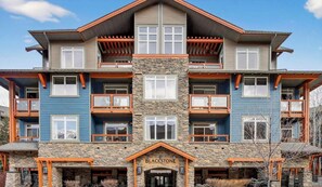 A multi-story building with a stone facade, multiple balconies, and a prominent entrance labeled "Blackstone." - Blackstone Luxe | Sleeps 8 | Pool & Hot Tubs | AC (Canmore)