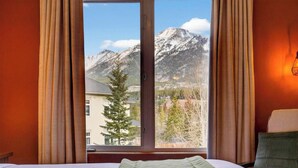 Una camera d'hotel con un letto, una finestra con tende e vista sulle montagne innevate.