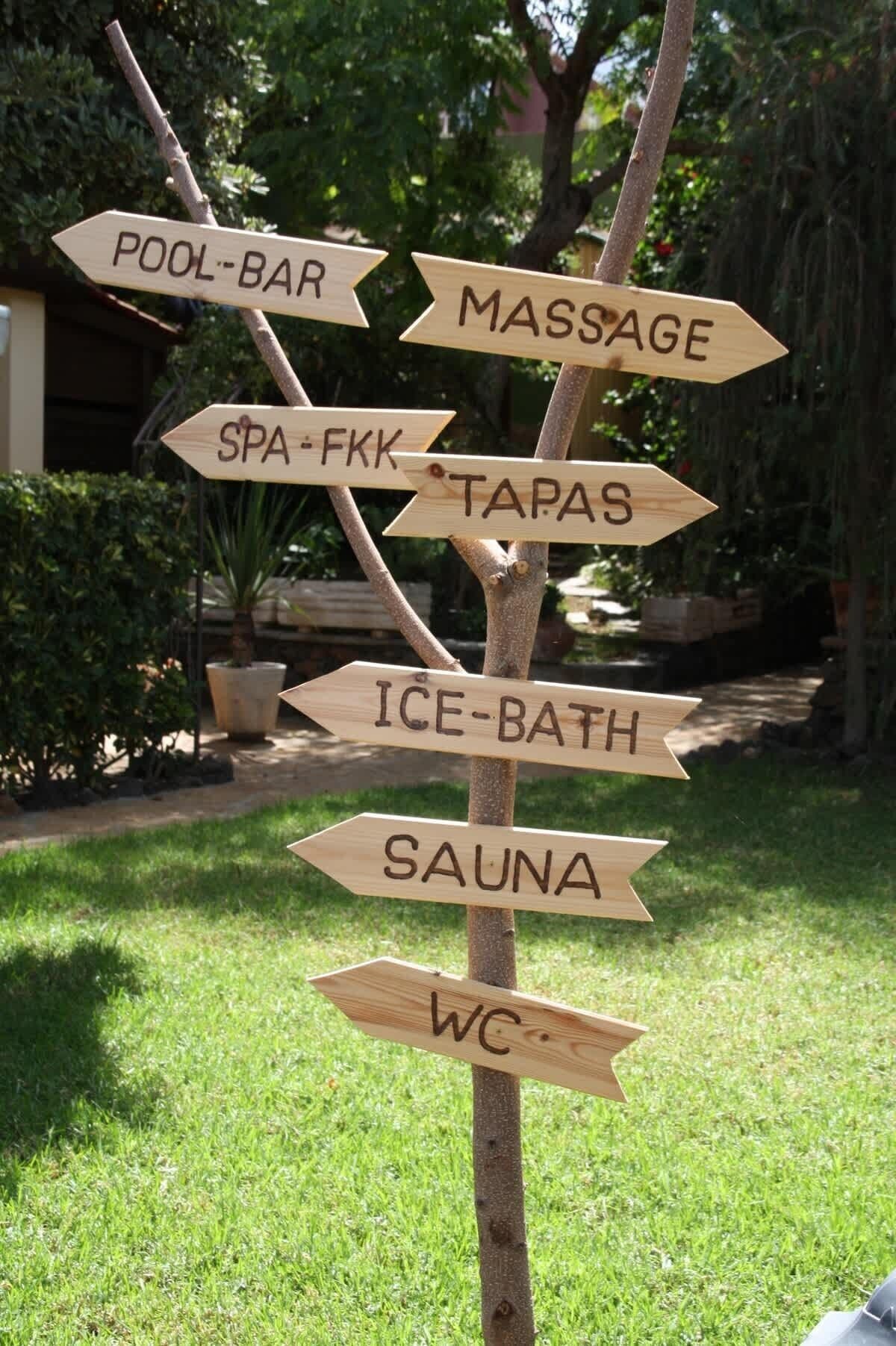A wooden signpost with directions to various amenities including a pool-bar, massage, spa, tapas, ice-bath, sauna, and WC.