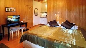 Un dormitorio con cama, escritorio, televisor, zona de cocina y paredes de madera.