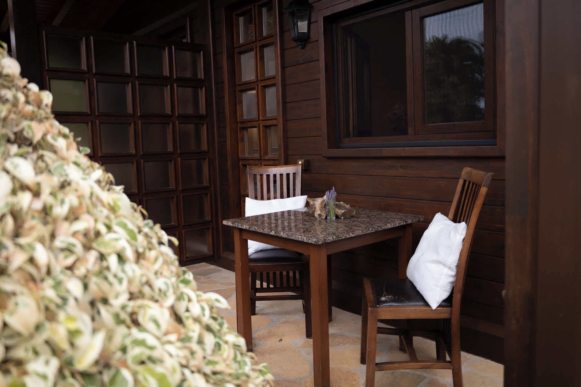 A wooden table and chairs set outside a building with large windows and a stone floor.