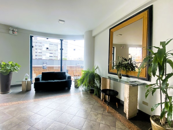 A spacious living area with a black sofa, a large mirror, and multiple potted plants. - Confortable 2 BR departamento Miraflores (Lima)