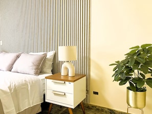 A bed with pillows, a bedside table with a lamp, a drawer, a potted plant, and a striped wall. - Confortable 2 BR departamento Miraflores (Lima)