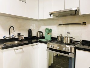 A kitchen with white cabinets, a black countertop, a stove, a coffee maker, and a kettle. - Confortable 2 BR departamento Miraflores (Lima)