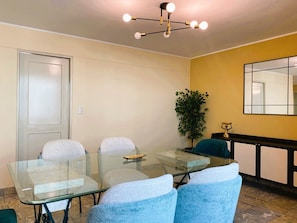 A dining area with a glass table and chairs, a potted plant, a mirror, and a ceiling light fixture. - Confortable 2 BR departamento Miraflores (Lima)