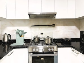 A kitchen with white cabinets, a stove, and a coffee maker. - Confortable 2 BR departamento Miraflores (Lima)