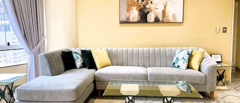 Una sala moderna con un sofá seccional gris, una mesa de centro de vidrio y un cuadro en la pared.