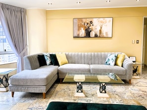 A modern living room with a grey sectional sofa, a glass coffee table, and a painting on the wall. - Confortable 2 BR departamento Miraflores (Lima)
