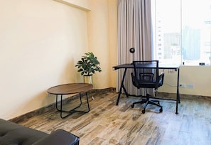 A room with a wooden table, a black office chair, a potted plant, and a view of buildings through a window with curtains. - Confortable 2 BR departamento Miraflores (Lima)