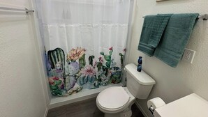 Un baño con cortina de ducha con diseño de cactus y flores, un inodoro y un perchero con una toalla verde.