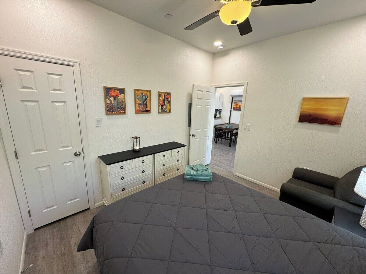 A bedroom with a large bed, a dresser, a ceiling fan, and a door leading to another room.