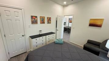 A bedroom with a large bed, a dresser, a ceiling fan, and a door leading to another room.