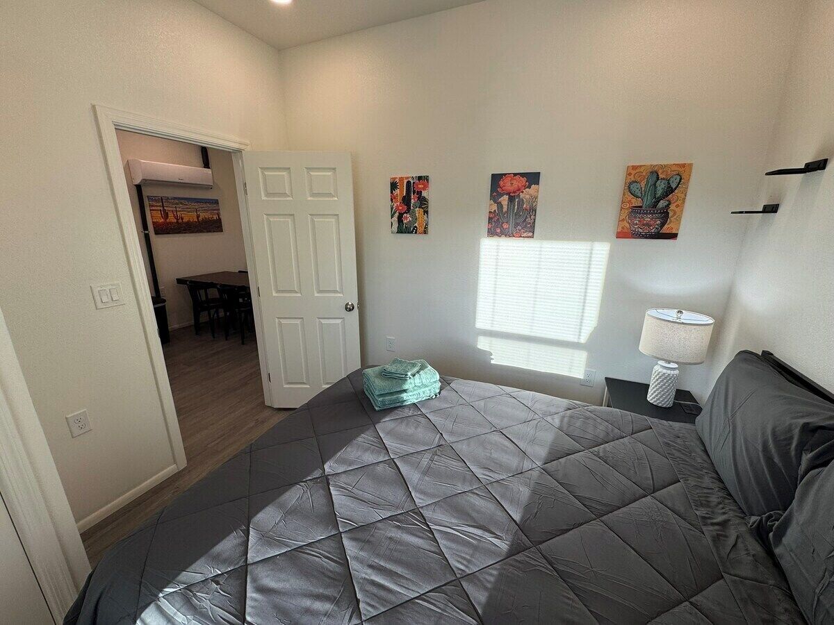 Een slaapkamer met een groot bed, een deur naar een eethoek en drie wanddecoraties.
