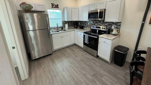 Cocina compacta con armarios blancos, electrodomésticos de acero inoxidable y salpicadero de azulejos.