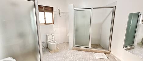 A bathroom with a toilet, a shower with a glass door, and a tiled floor.