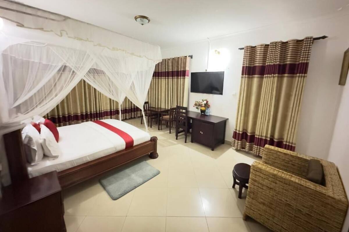 A hotel room with a bed, a desk, a television, and a wicker chair.