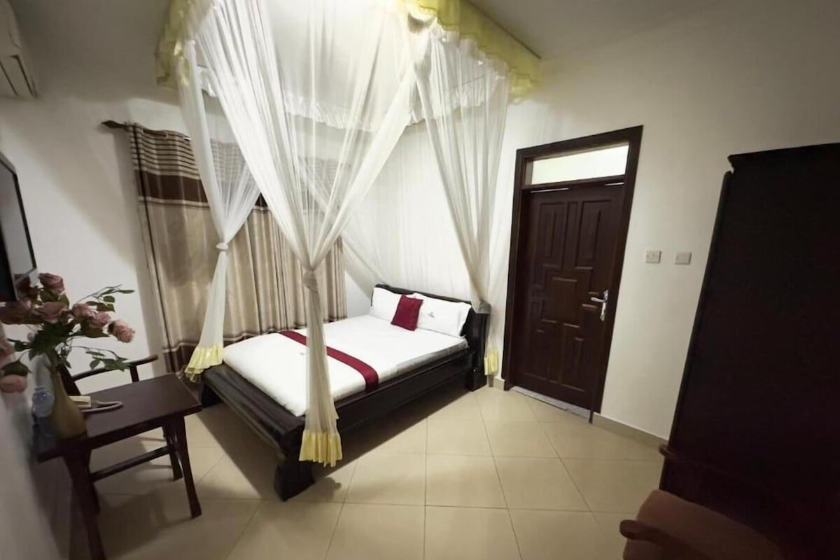Quarto com cama, mesa de cabeceira, cadeira, porta e janela.