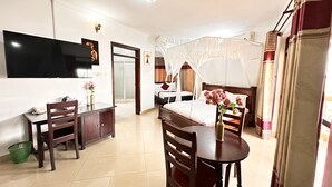 A hotel room with a bed, a TV, a dining table, and a chair.