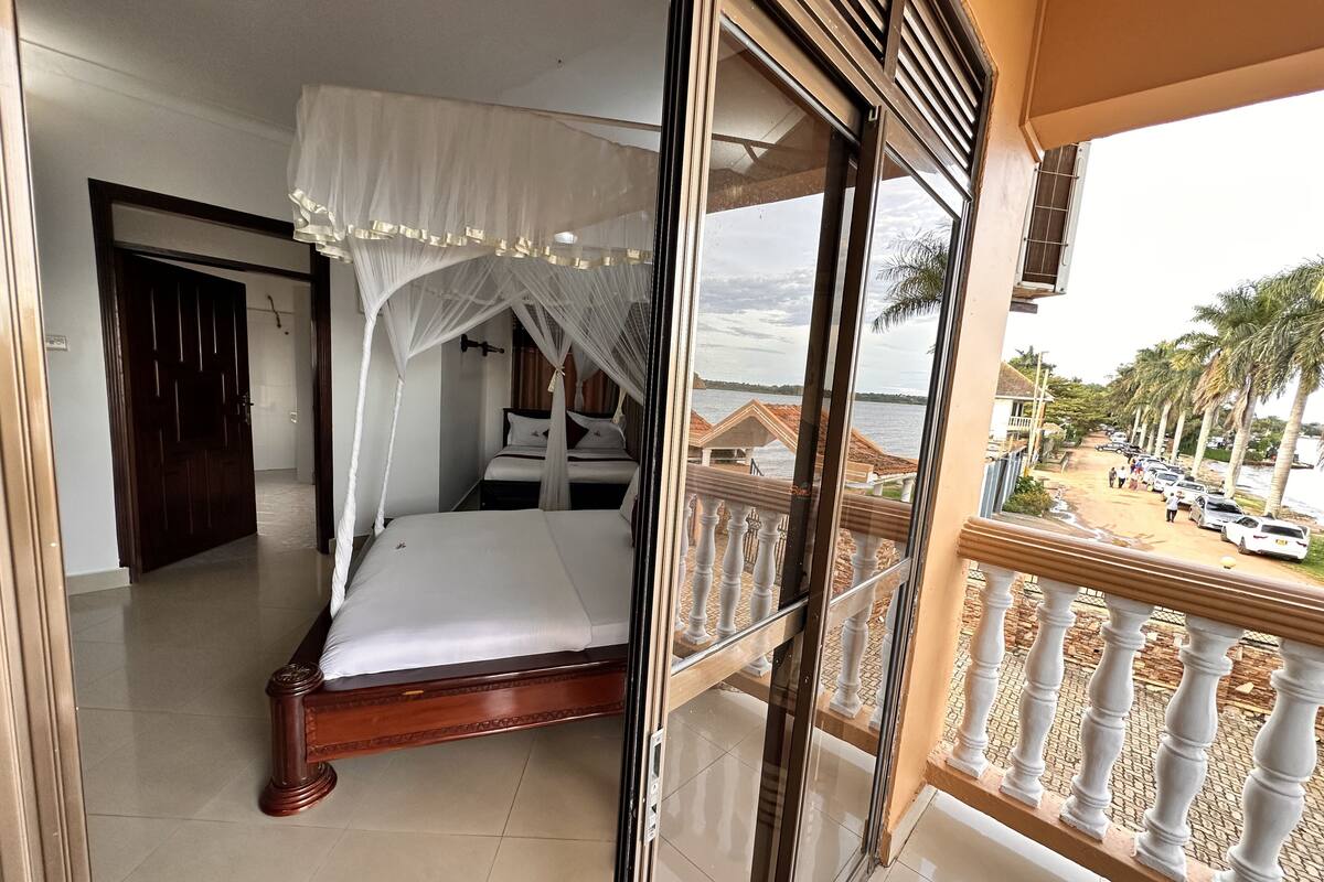 A bedroom with a bed, a window with a view of a beach and palm trees.