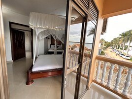 Un dormitorio con cama, ventana y vista a una playa y palmeras.