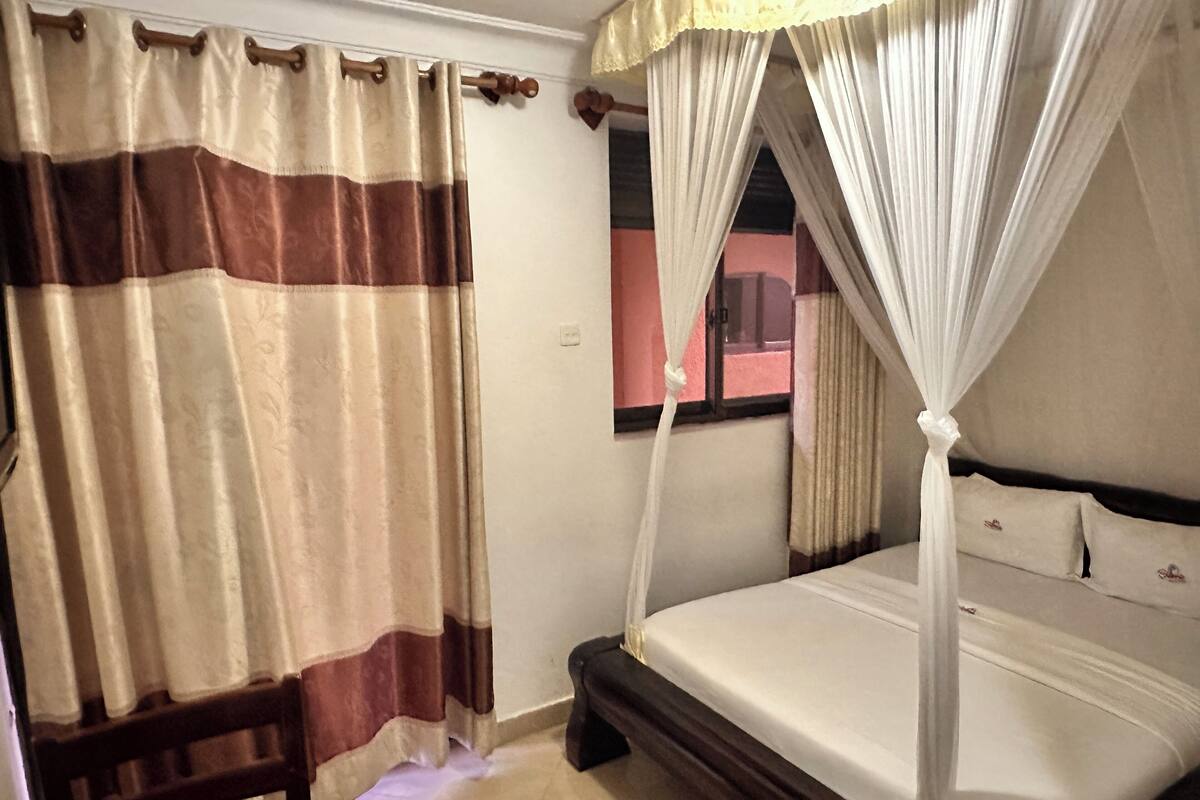 A bedroom with a bed, curtains, a chair, and a window with a view.
