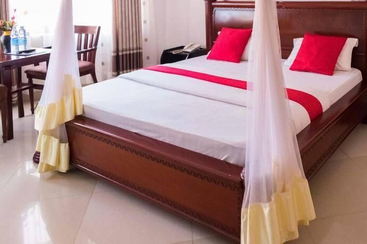 A bed with a canopy, a bedside table, and a chair in a hotel room.