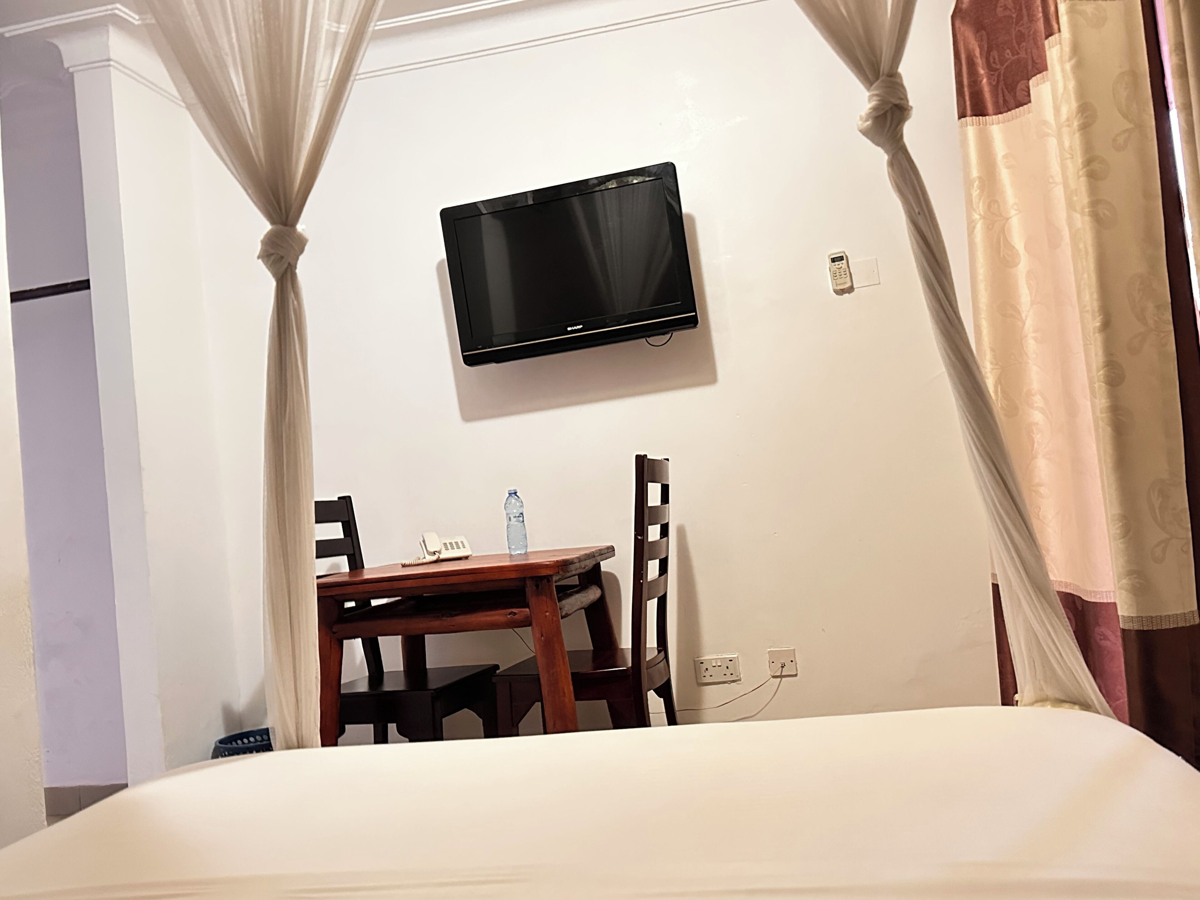 A hotel room with a bed, a desk with a chair, a television mounted on the wall, and a telephone.