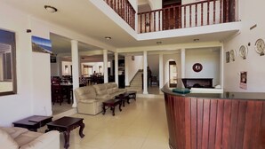 A spacious lobby with a high ceiling, a reception desk, a sofa, and a staircase leading to an upper floor.