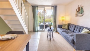 A modern living room with a staircase, a dining table set with plates and a glass, a grey sofa with cushions, and a dining table with chairs. - Clos Fontaine House with garden, pool (Valras-Plage)
