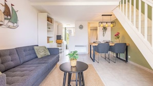 A modern living room with a sofa, a small round table, and a dining area with chairs. - Clos Fontaine House with garden, pool (Valras-Plage)